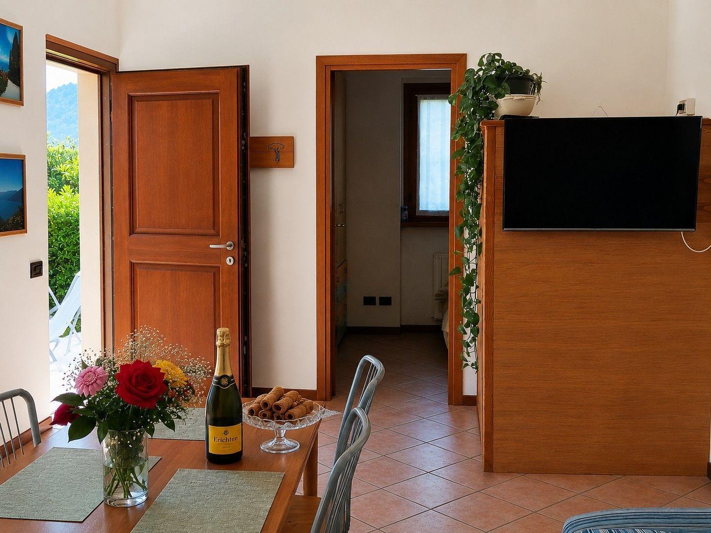 Esszimmer mit Tisch, Stühlen, Blumen und Flasche. Durchgang zu Schlafzimmer und Terrasse.