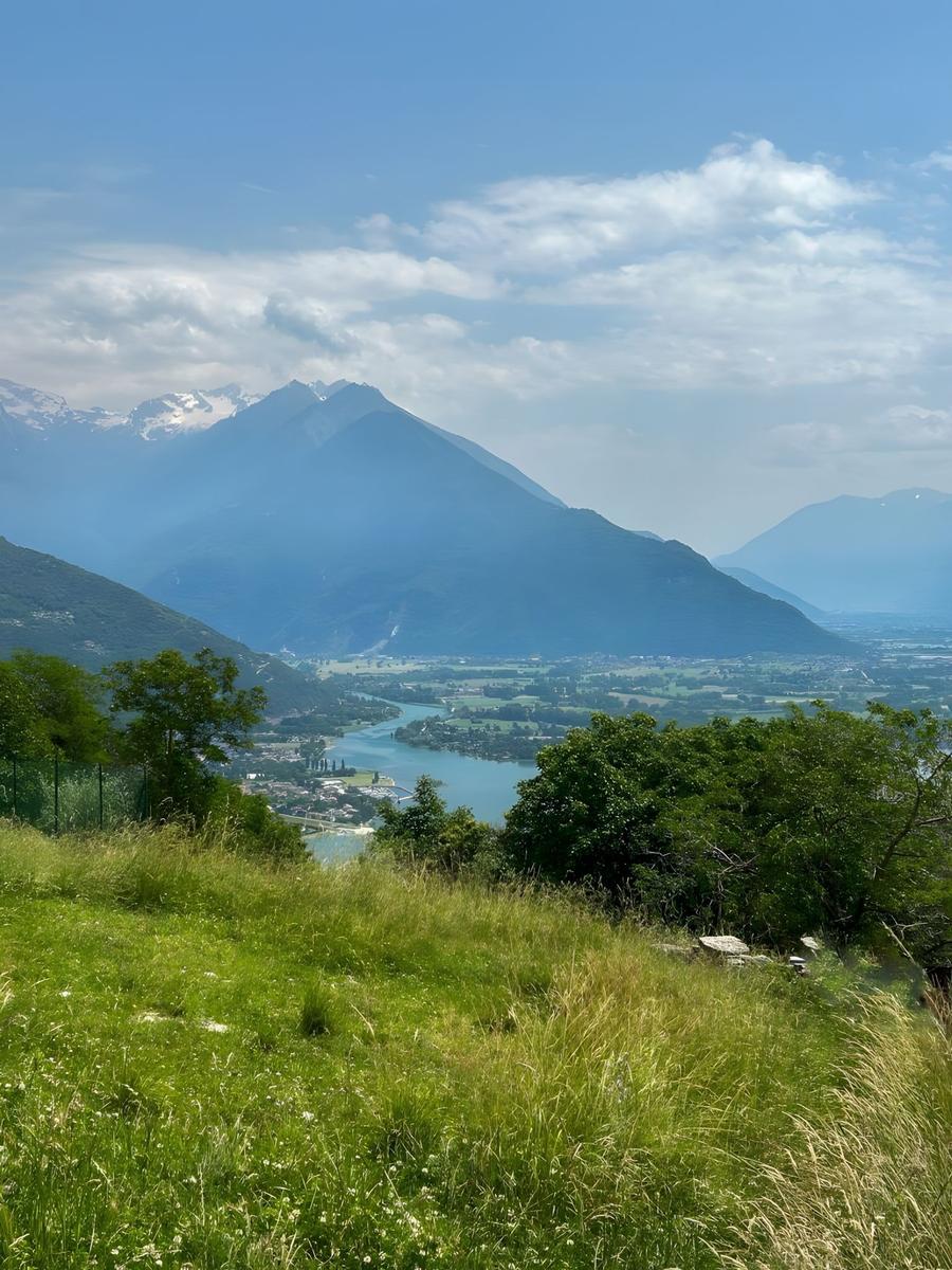 Panoramablick auf See und Berge mit grüner Wiese im Vordergrund.