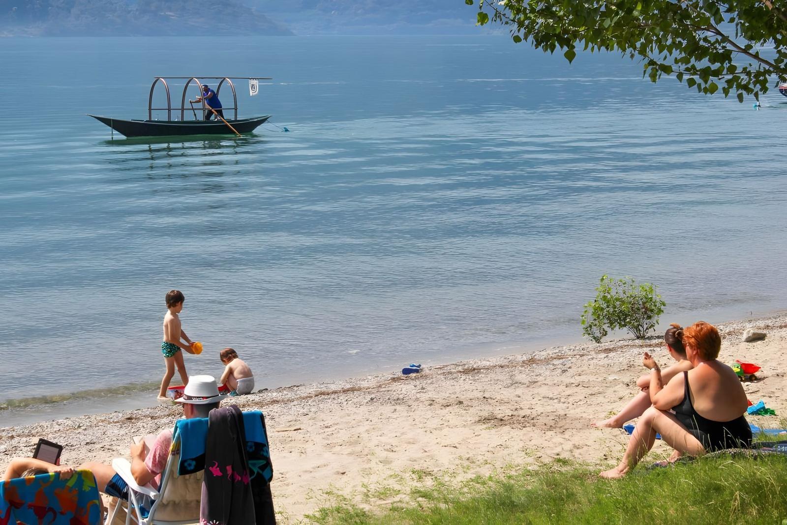 Strand mit Kindern, Erwachsenen und einem Boot im Wasser.