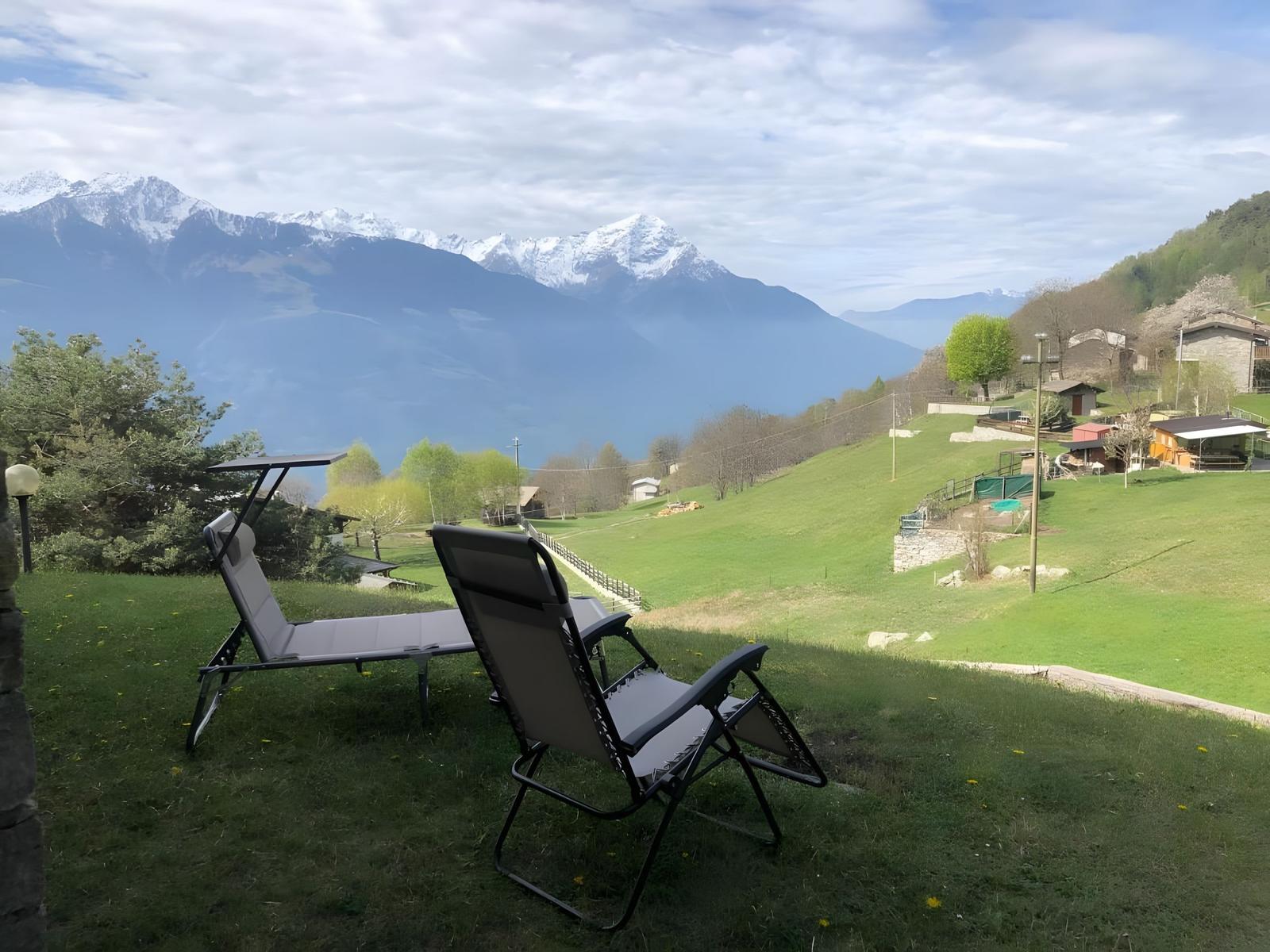 Zwei Liegestühle auf einer grünen Wiese mit Blick auf schneebedeckte Berge.
