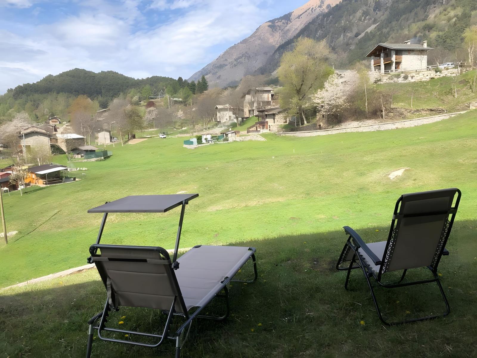 Zwei Liegestühle auf einer grünen Wiese mit Blick auf Berge und Häuser.
