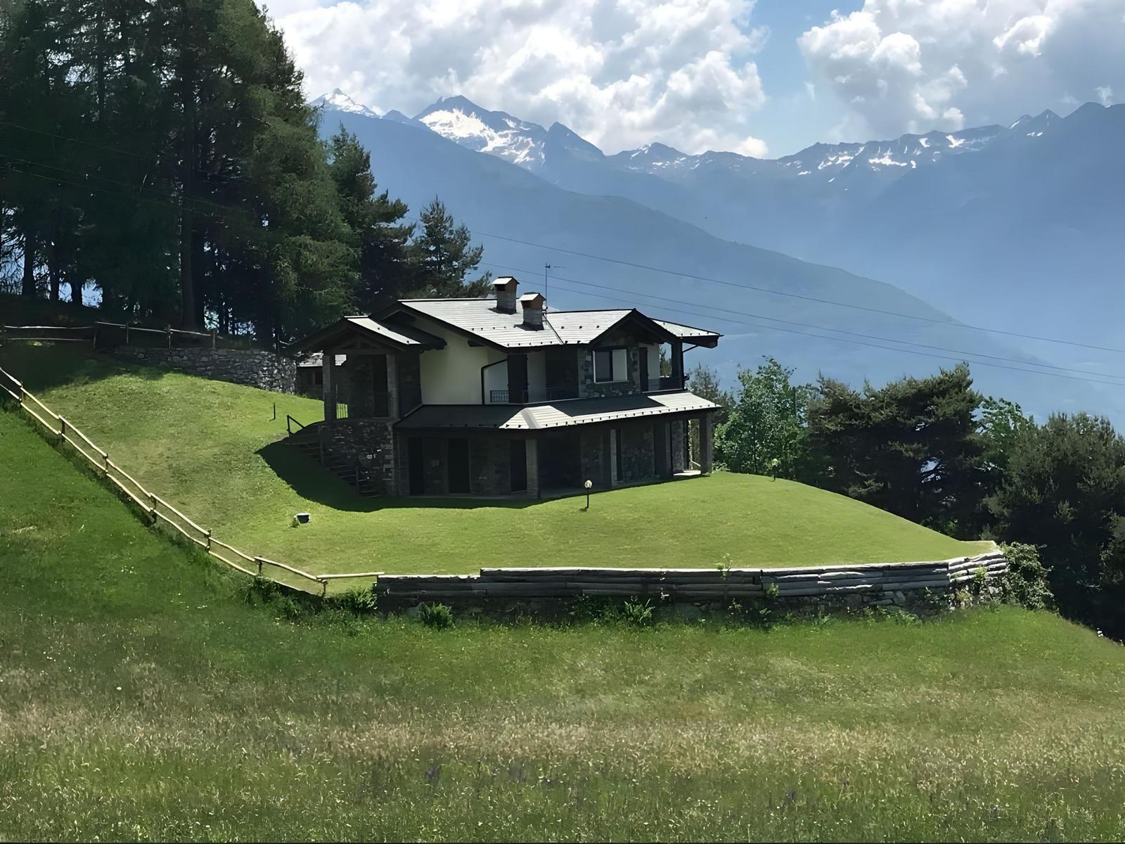 Haus auf grünem Hang mit Bergblick und Wald umgeben