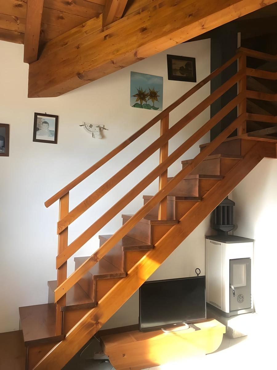 Holzstiege mit Geländer führt zur oberen Etage. Wand mit Bildern und Ofen.