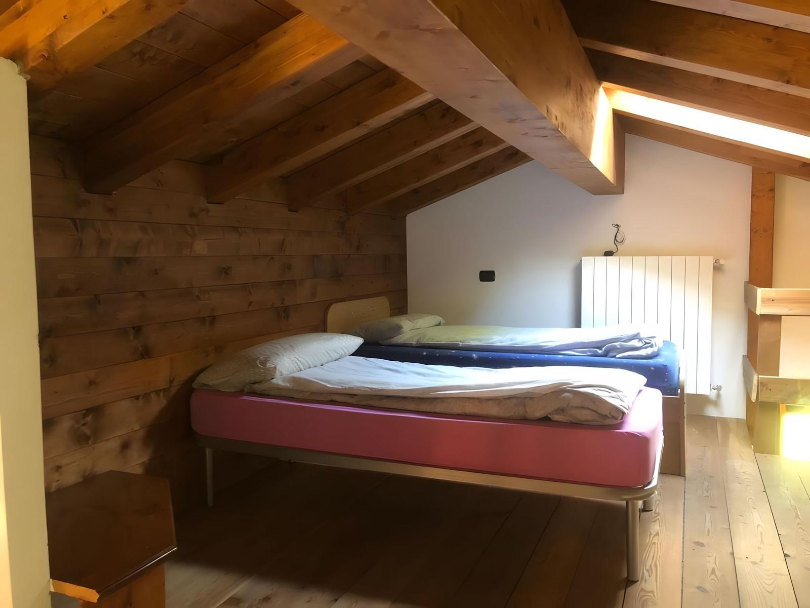 Zwei Betten in einem Dachzimmer mit Holzwand und -decke.