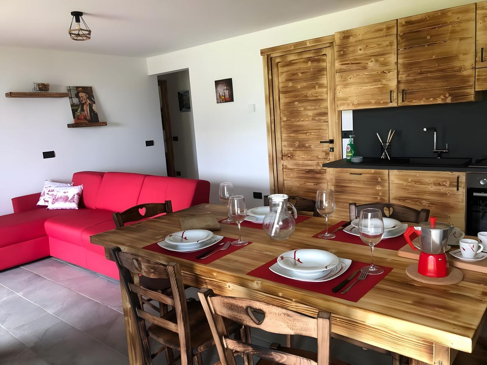 Essbereich mit Holztisch, Stühlen und rotem Sofa. Küche mit Holzschränken und schwarzer Arbeitsfläche.