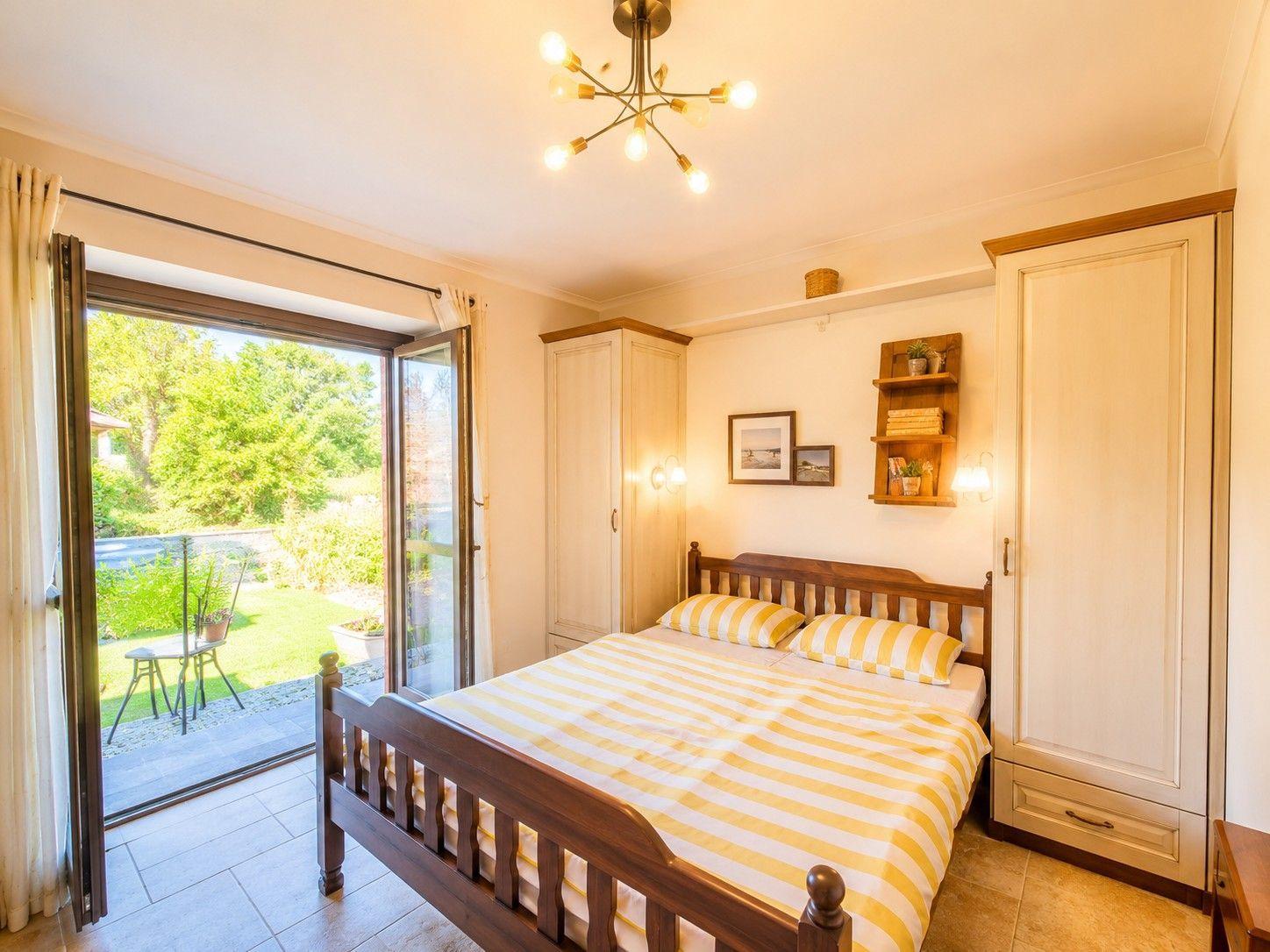 Schlafzimmer mit Bett, Schränken und Terrassentür. Blick auf grünen Garten.