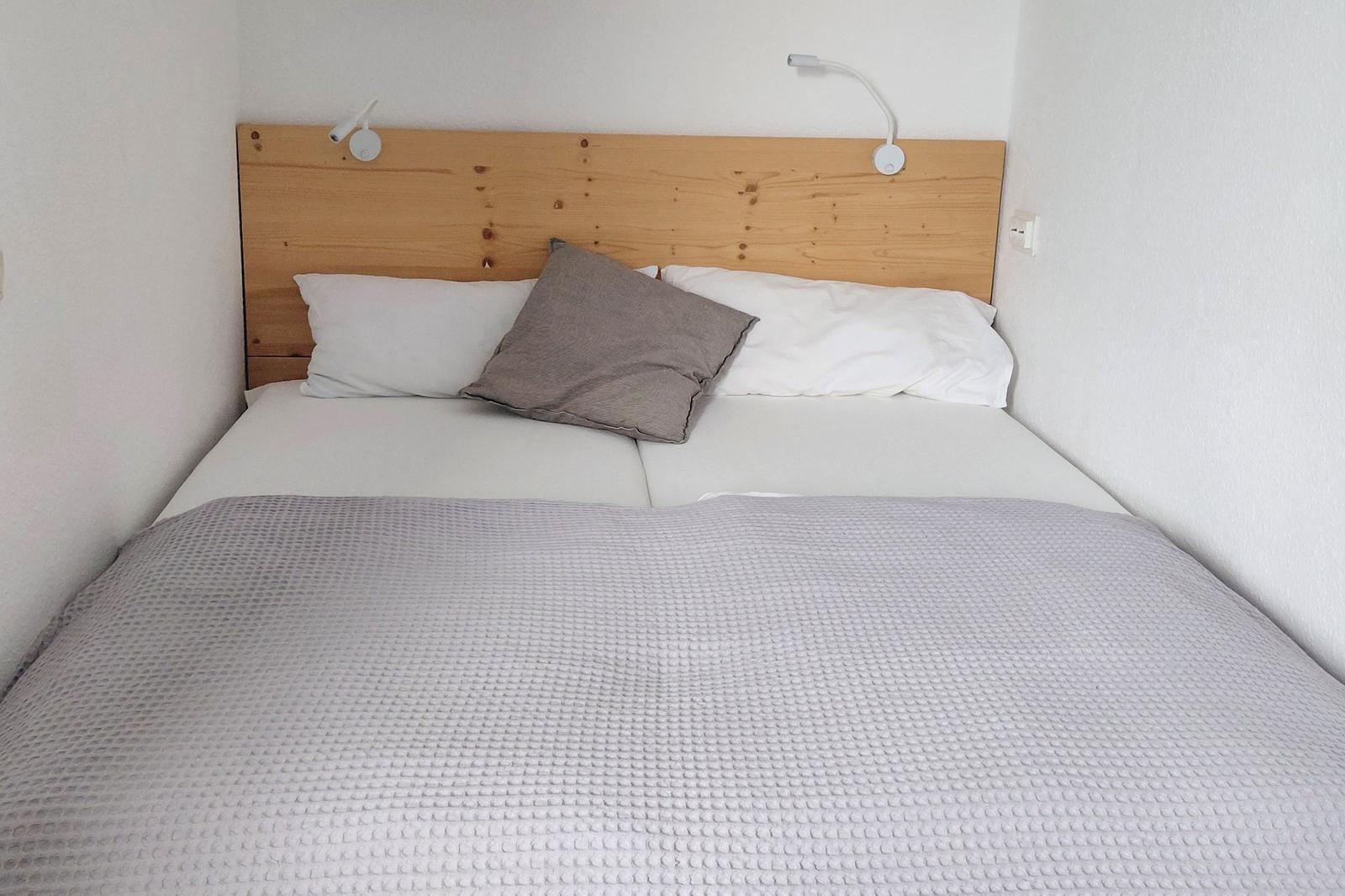 Ein Bett mit Holz-Kopfteil, weißen Kissen und grauer Decke.