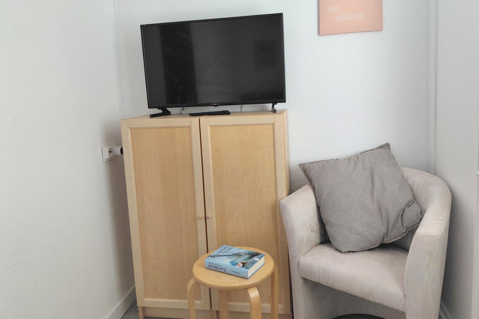 Ein kleiner Raum mit einem Stuhl, einem TV und einem Tisch mit Buch.