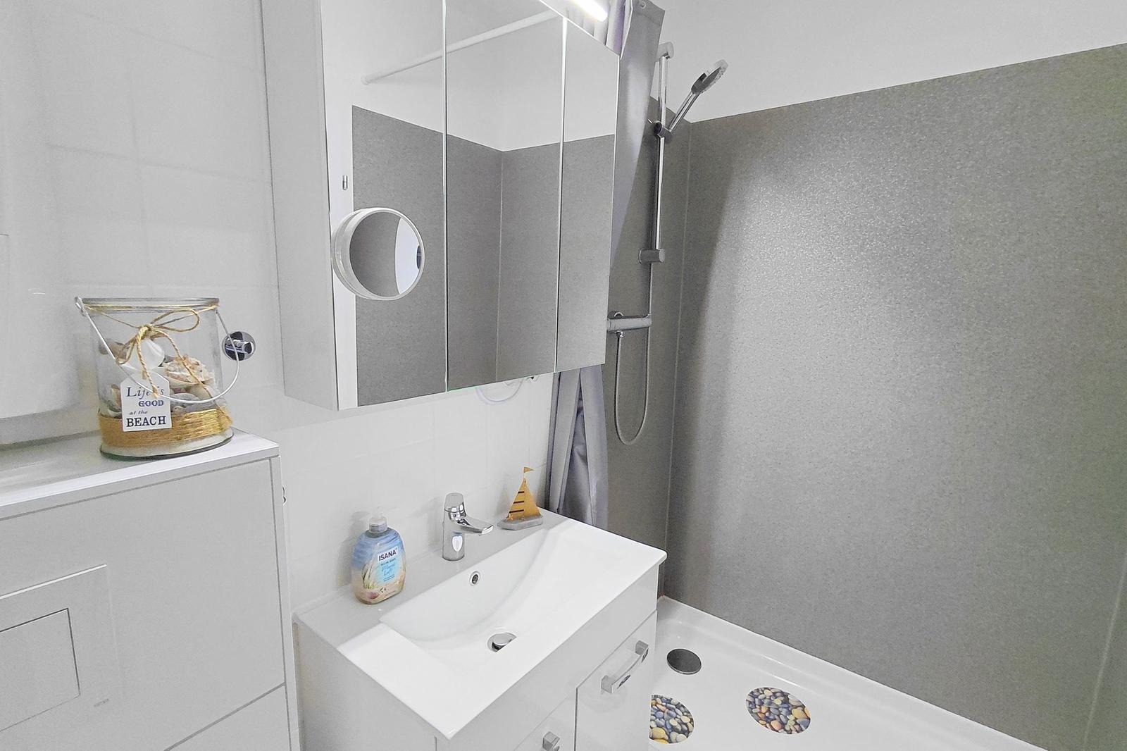 Badezimmer mit Dusche, Waschbecken und Spiegelschrank. Auf dem Waschtisch steht eine Seebade-Dekoration.