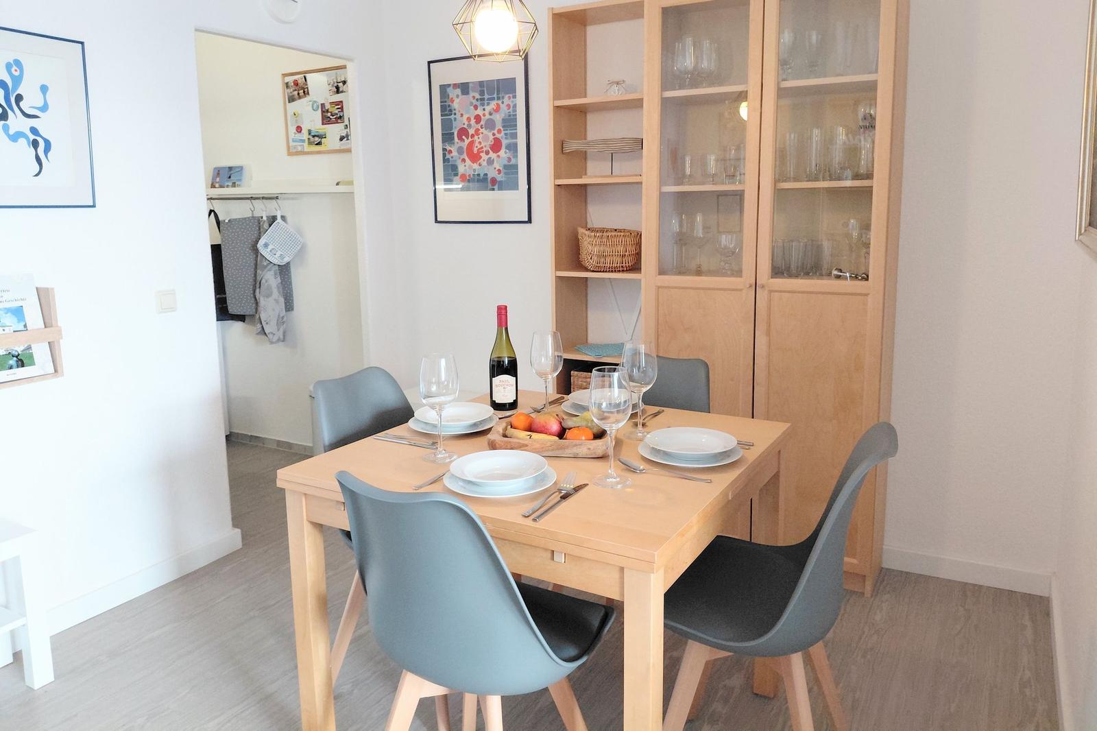 Esszimmer mit Holztisch, Stühlen und Glasvitrine. Tisch gedeckt mit Wein und Obst.