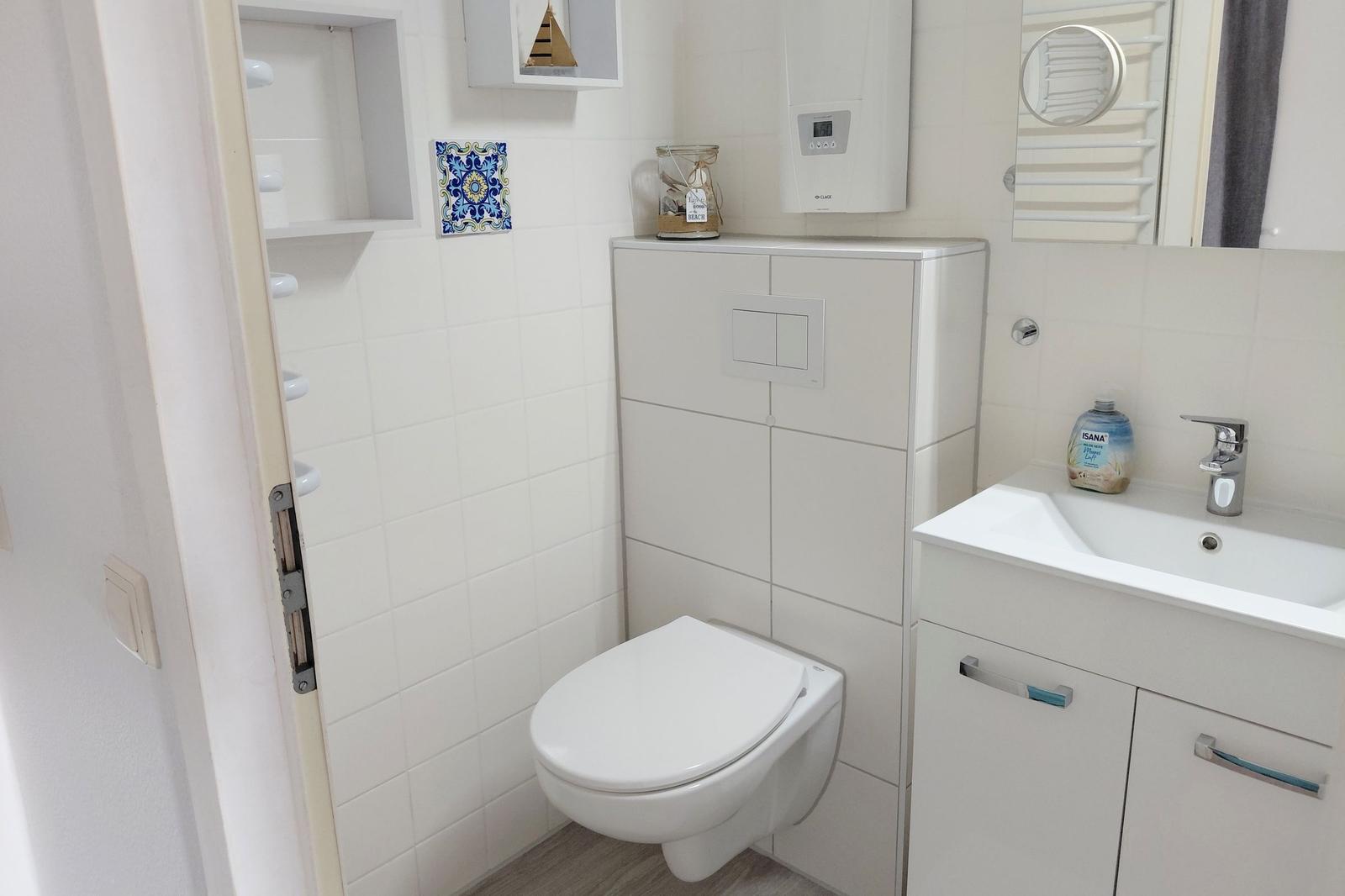 Badezimmer mit Toilette, Waschbecken und Heizung. Wandverkleidung und Spiegel sichtbar.
