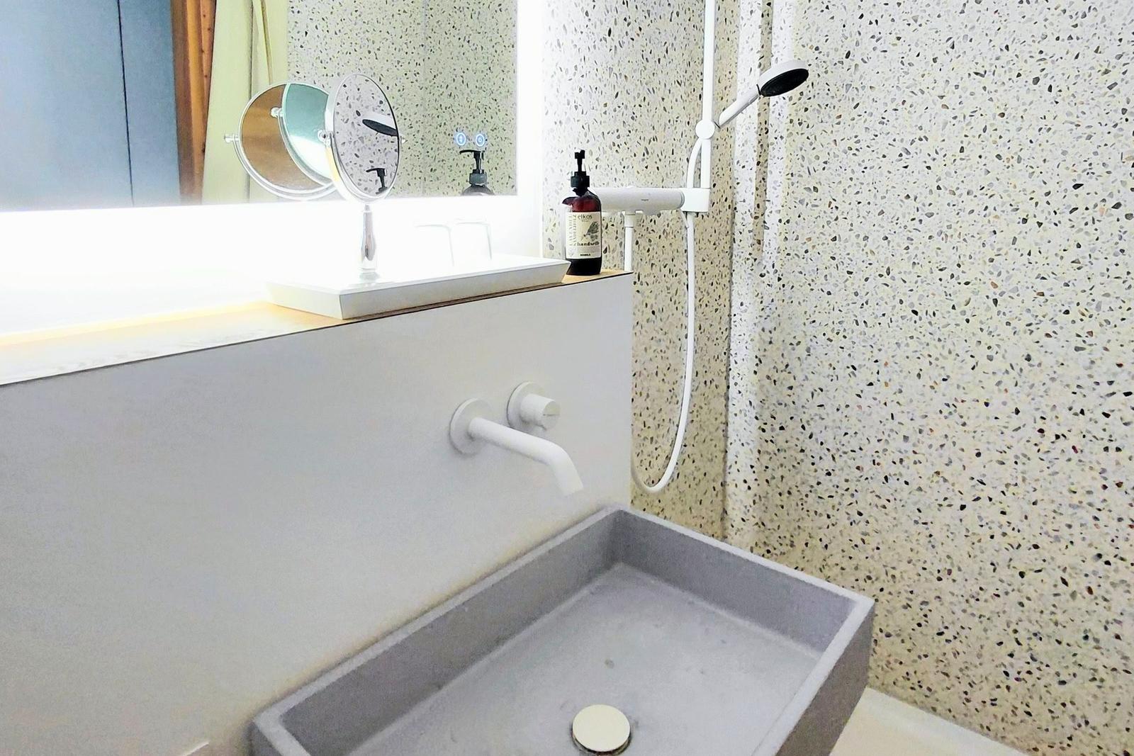Bad mit Dusche, Waschbecken und Spiegel. Wand mit Terrazzopflaster.