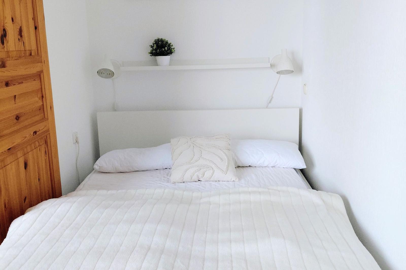 Ein Bett mit weißer Bettwäsche, Kopfteil und Nachttischlampen an der Wand.