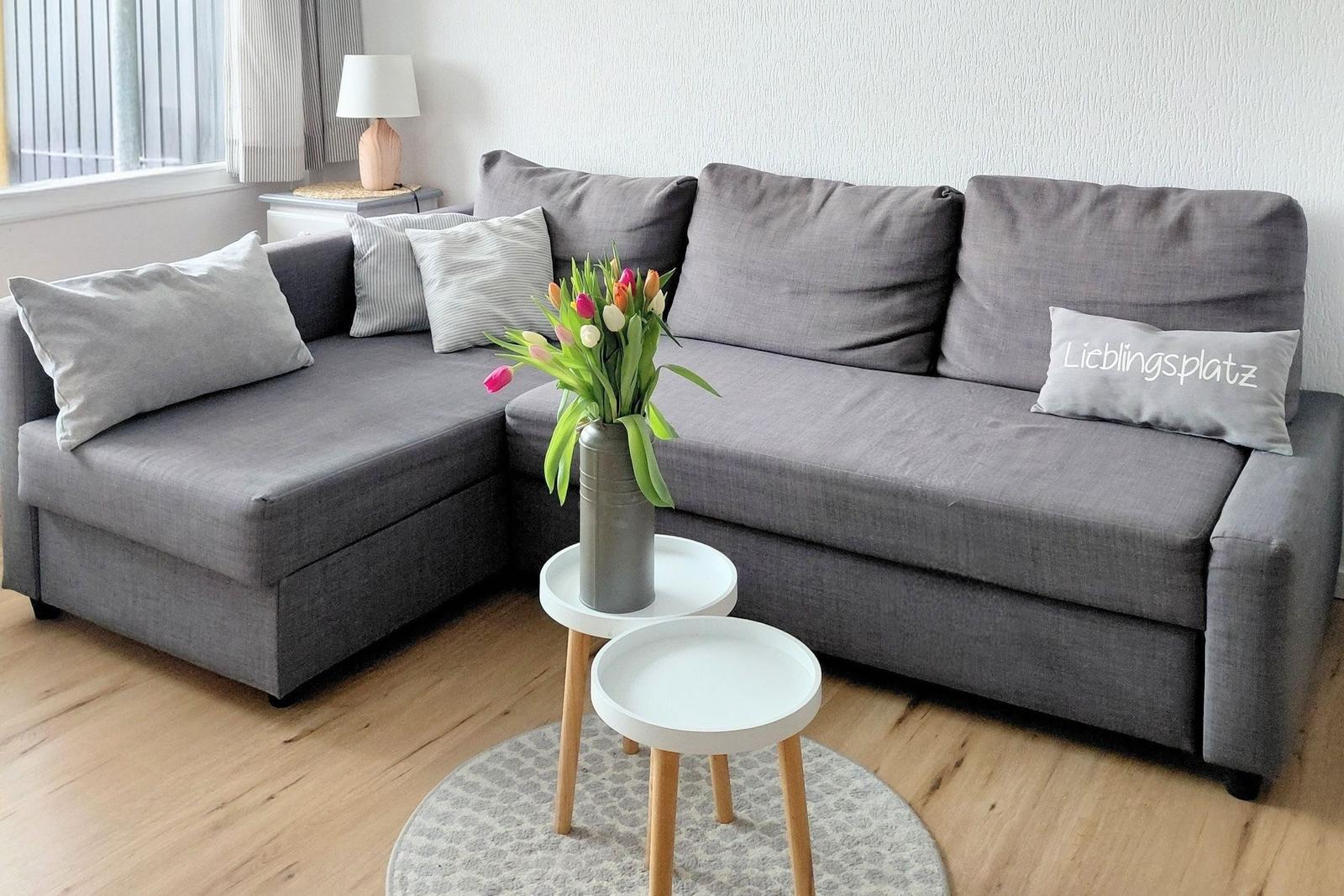 Graße Eckcouch mit Kissen, kleiner Tisch und Blumen im Wohnzimmer.