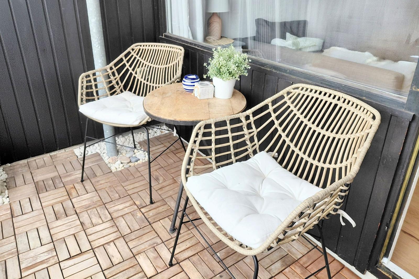 Terrasse mit zwei Stühlen und Tisch. Hintergrund: Fenster und dunkler Holzaufbau.