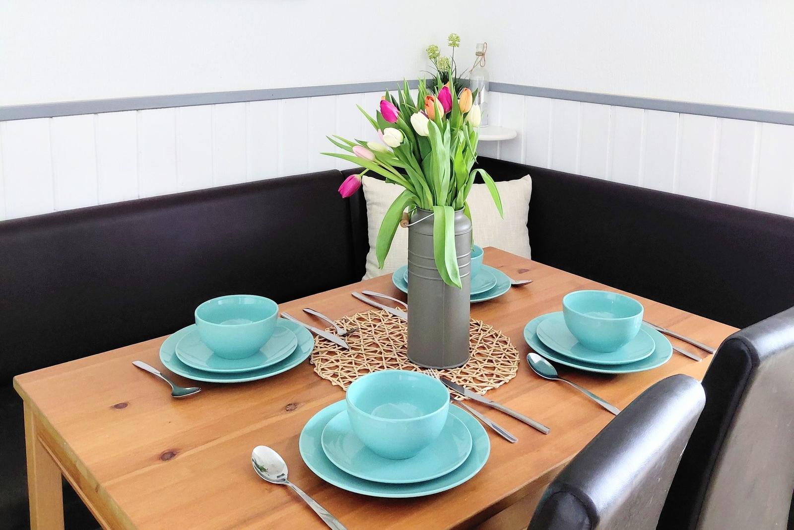 Holztisch mit blauer Geschirrset und Tulpen im Zentrum.