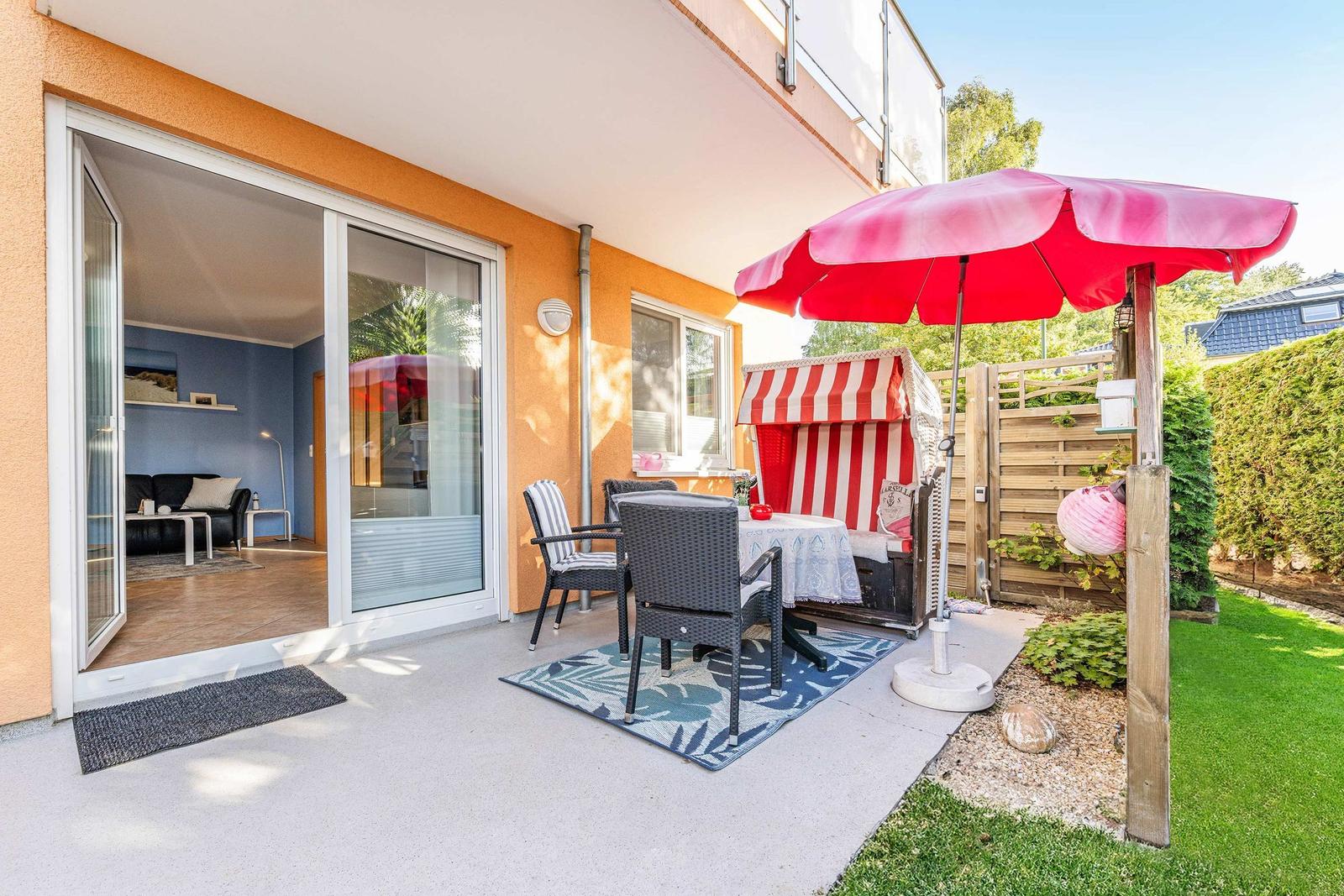 Terrace with table, chairs, and red umbrella. Sliding glass door leads to living room.