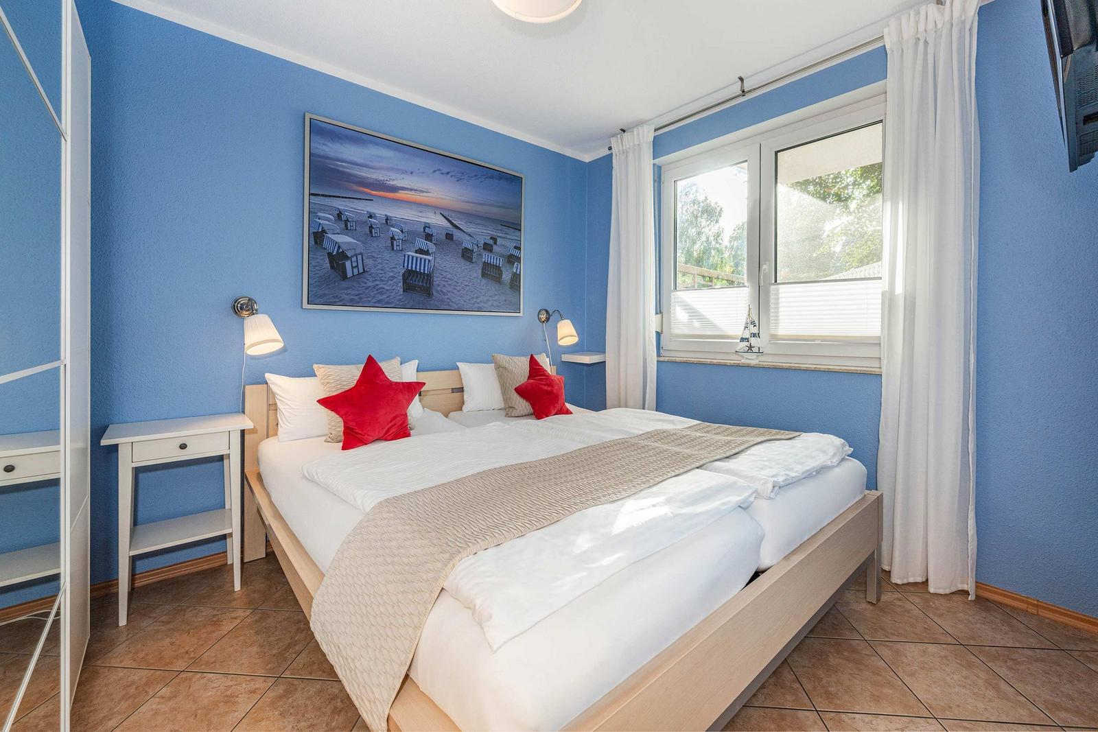 Bedroom with blue walls, bed with red pillows, and window with white curtains.