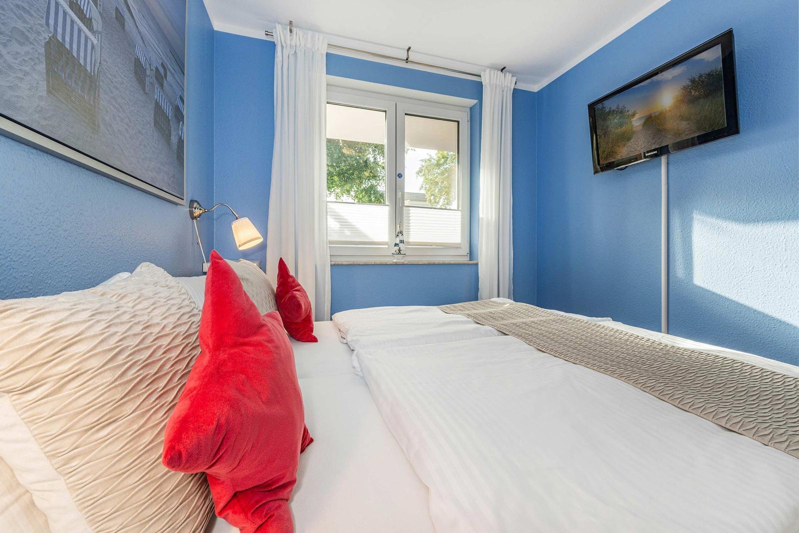 Bedroom with blue walls, bed with red pillows, and TV mounted on the wall.