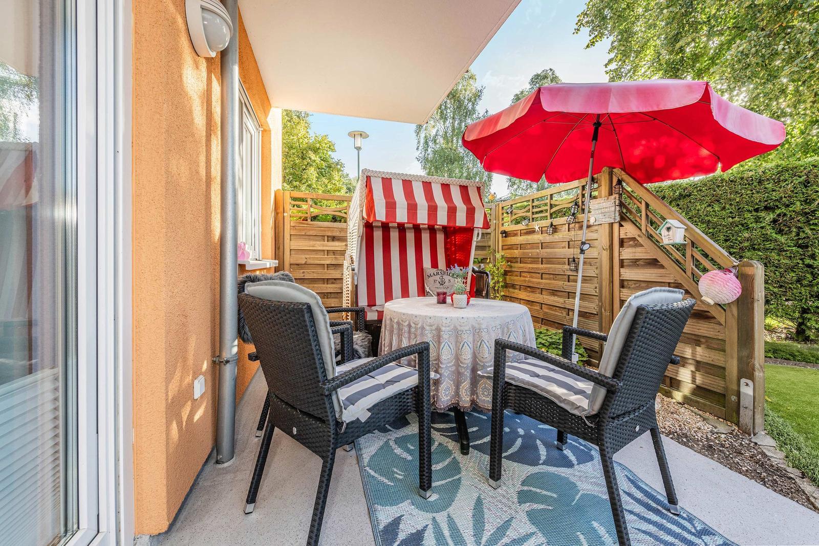 Terrace with table, two chairs, red umbrella, and beach cabana.
