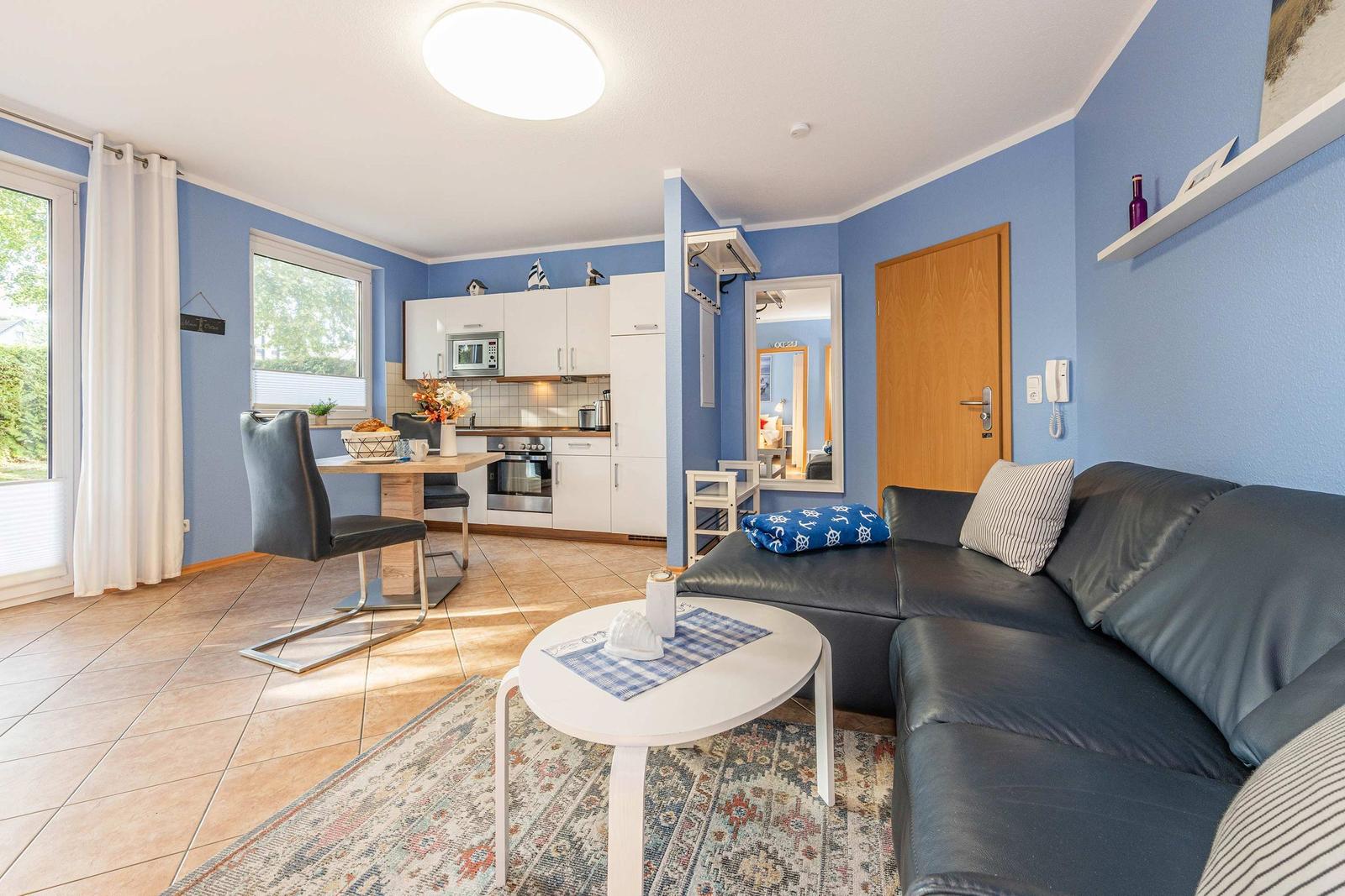 Living and dining area with kitchen, sofa, and table. Blue walls and wooden floor.