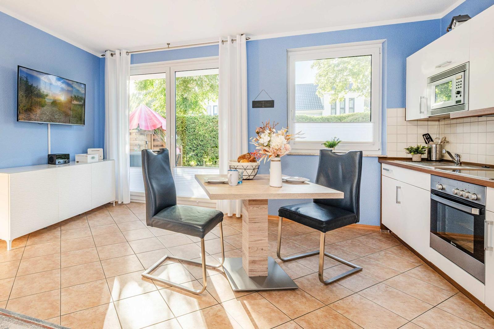 Kitchen and dining area with table, two chairs, TV, and view of the garden.