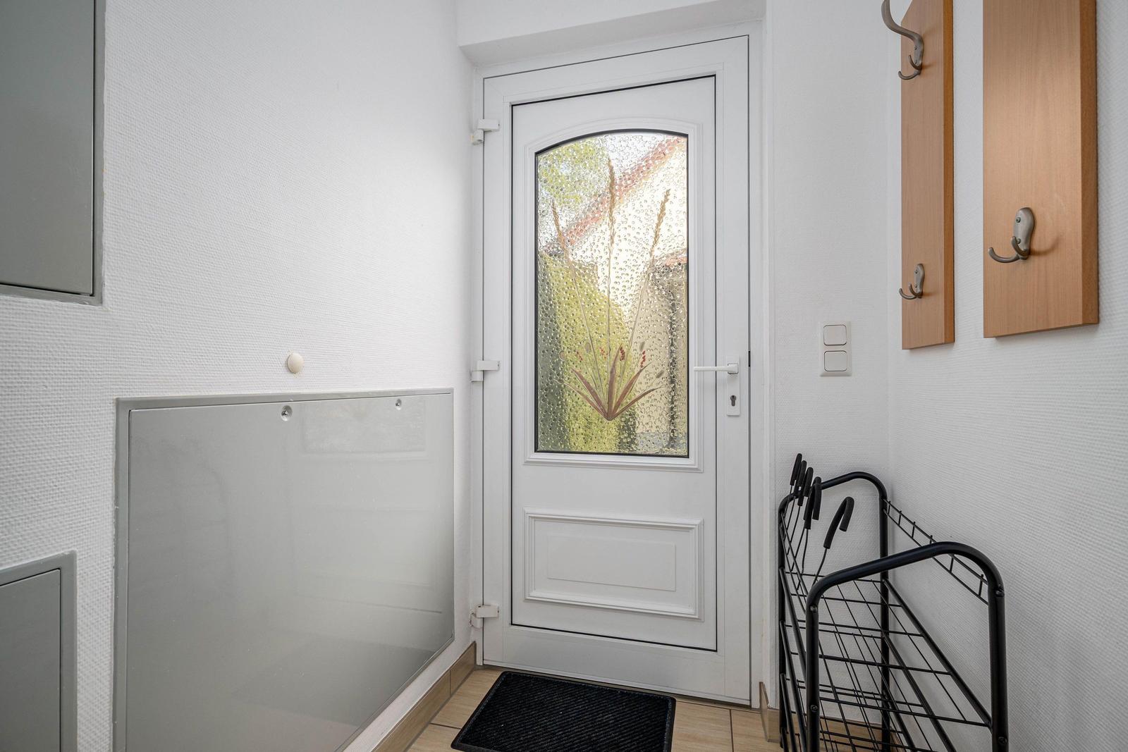 Eingangsbereich mit weißen Wänden, einer weißen Tür mit Glas und einem schwarzen Teppich.