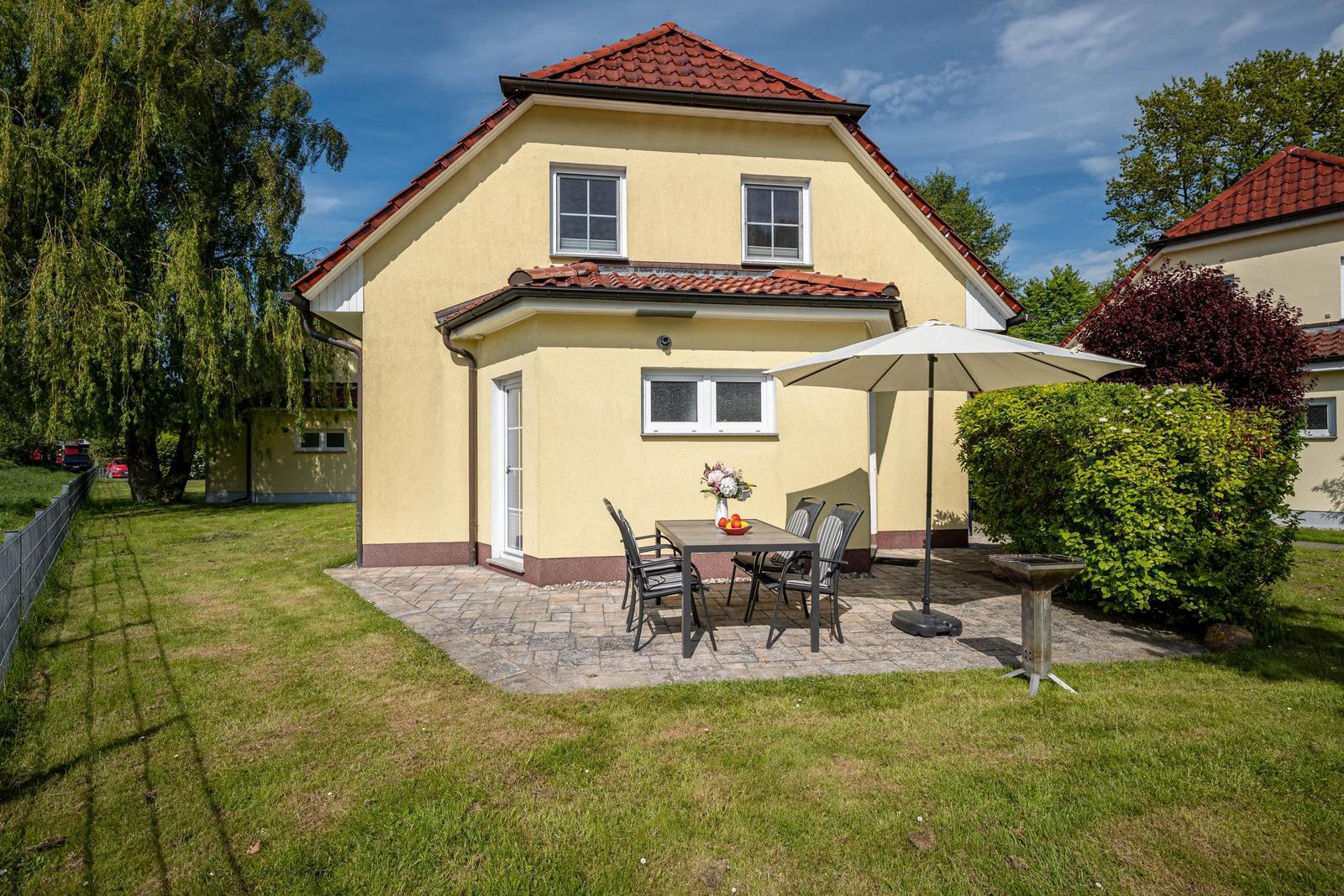 Haus mit Terrasse, Tisch, Stühlen und Sonnenschirm im Garten.