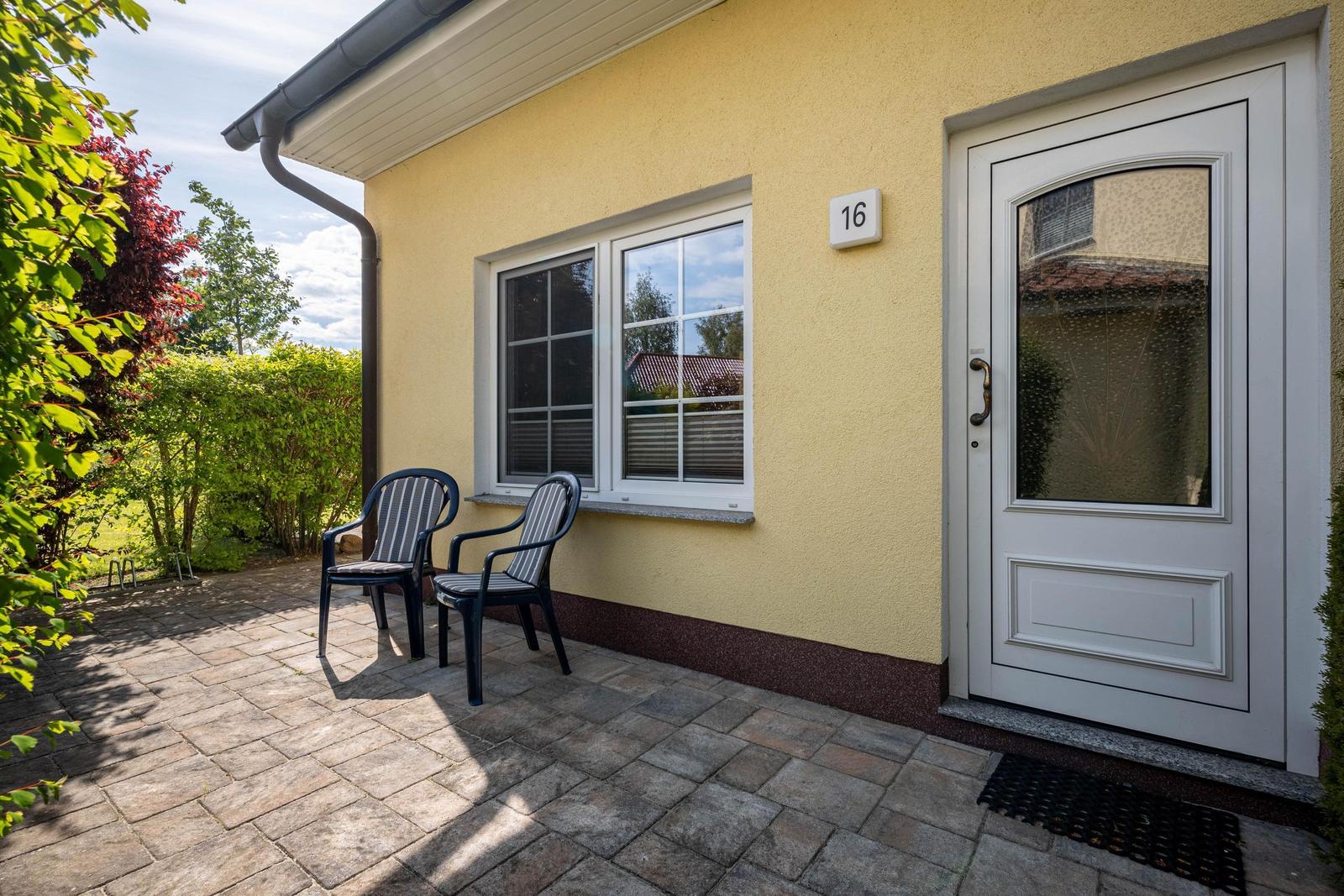 Haus mit Terrasse, zwei Stühlen und Eingangstür mit Nummer 16.