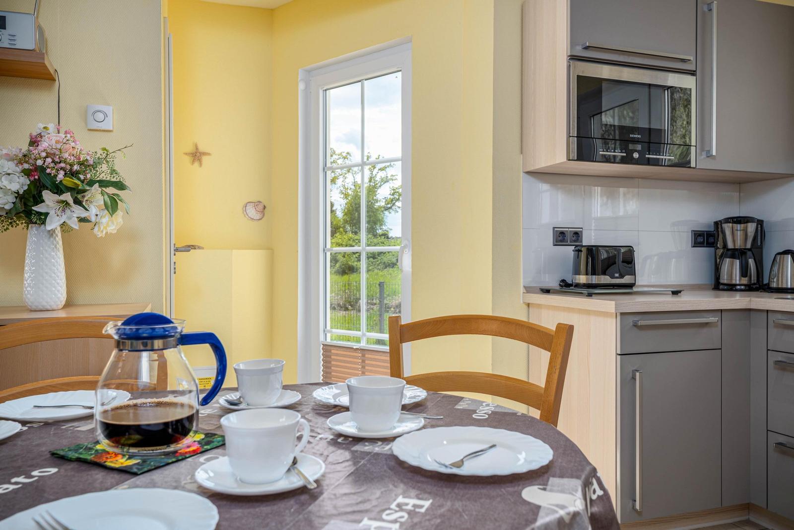 Esstisch mit Kaffeekanne und Tassen. Küchenzeile mit Mikrowelle und Fenster.