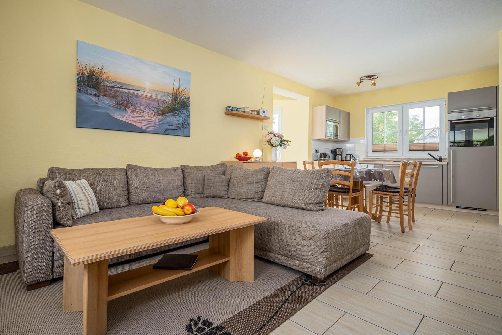 Wohnzimmer mit Sofa, Esstisch und Küche im Hintergrund.