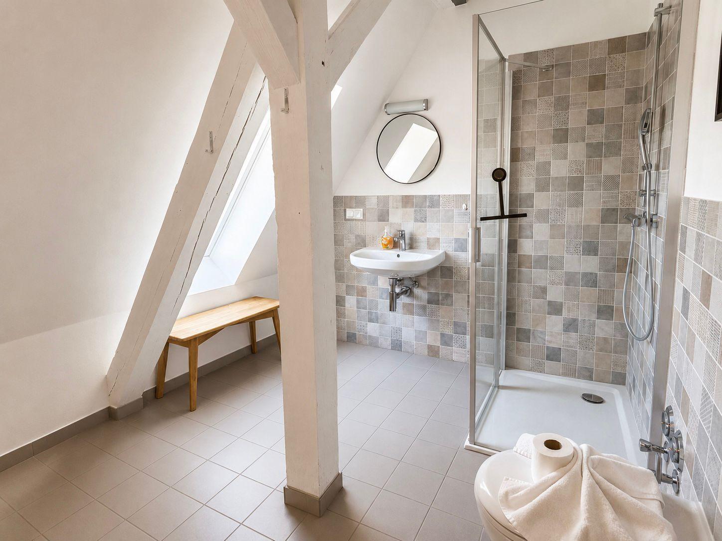 Dusche mit Glaswand, Waschbecken und Fenster im Dachgeschossbad.