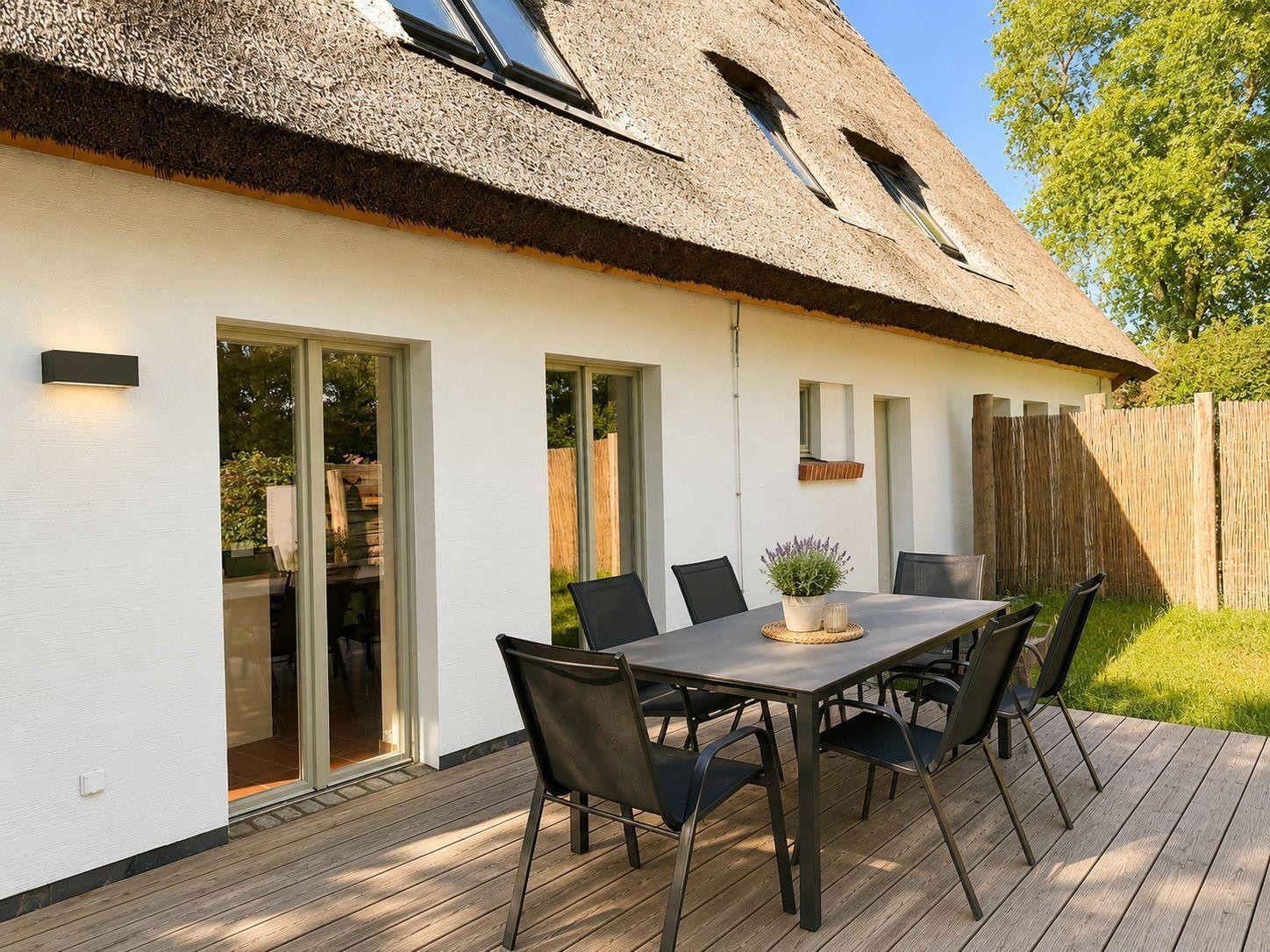 Terrasse mit Tisch und Stühlen vor einem Haus mit Strohdach und Schiebetüren.
