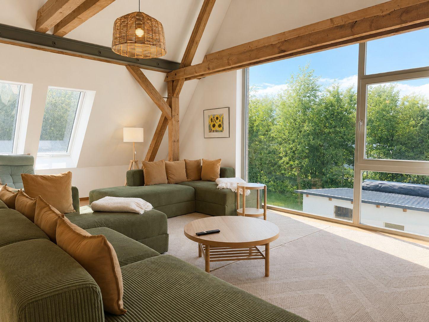 Wohnzimmer mit grünem Sofa, Holzrahmen und großem Fenster mit Blick auf Grünflächen.