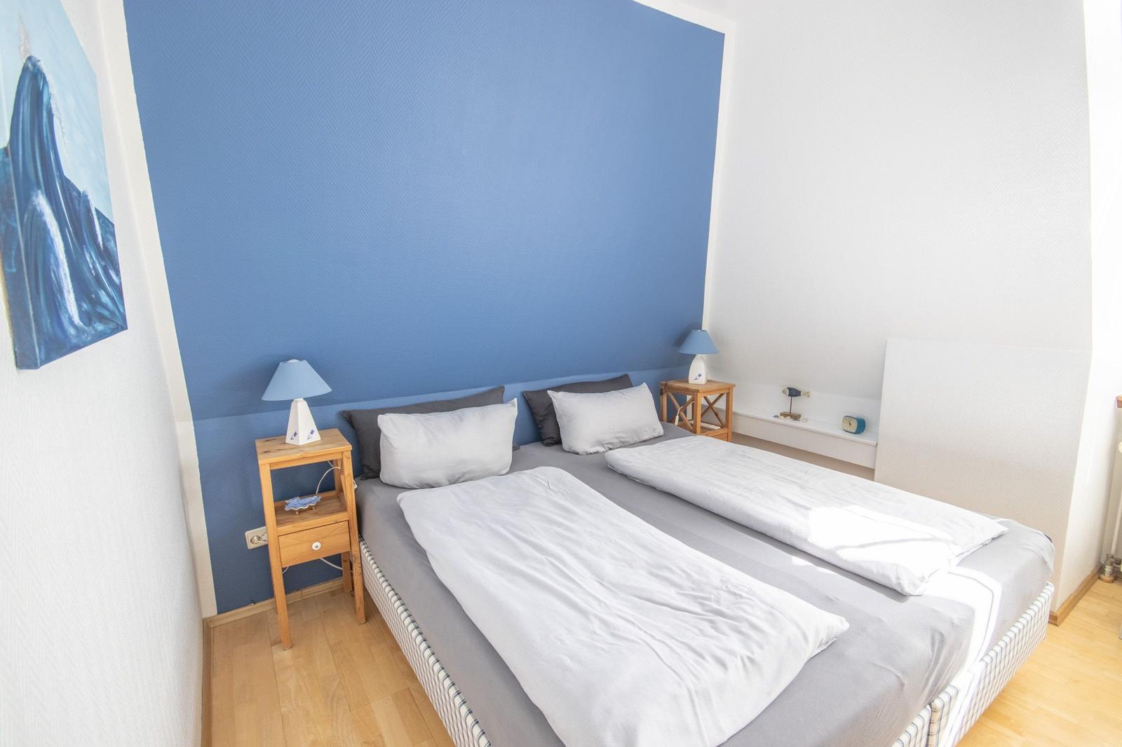 Schlafzimmer mit Doppelbett, blauer Wand und zwei Nachttischen.