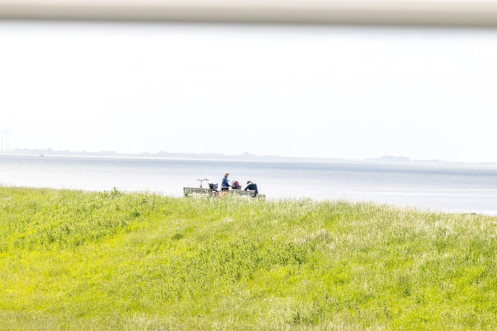 Zwei Personen sitzen am Ufer eines Sees mit Grasland im Vordergrund.