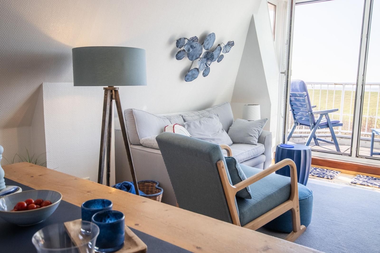 Wohnzimmer mit Sofa, Sessel und Balkonansicht. Holztisch, Stehlampe und Wanddekoration.
