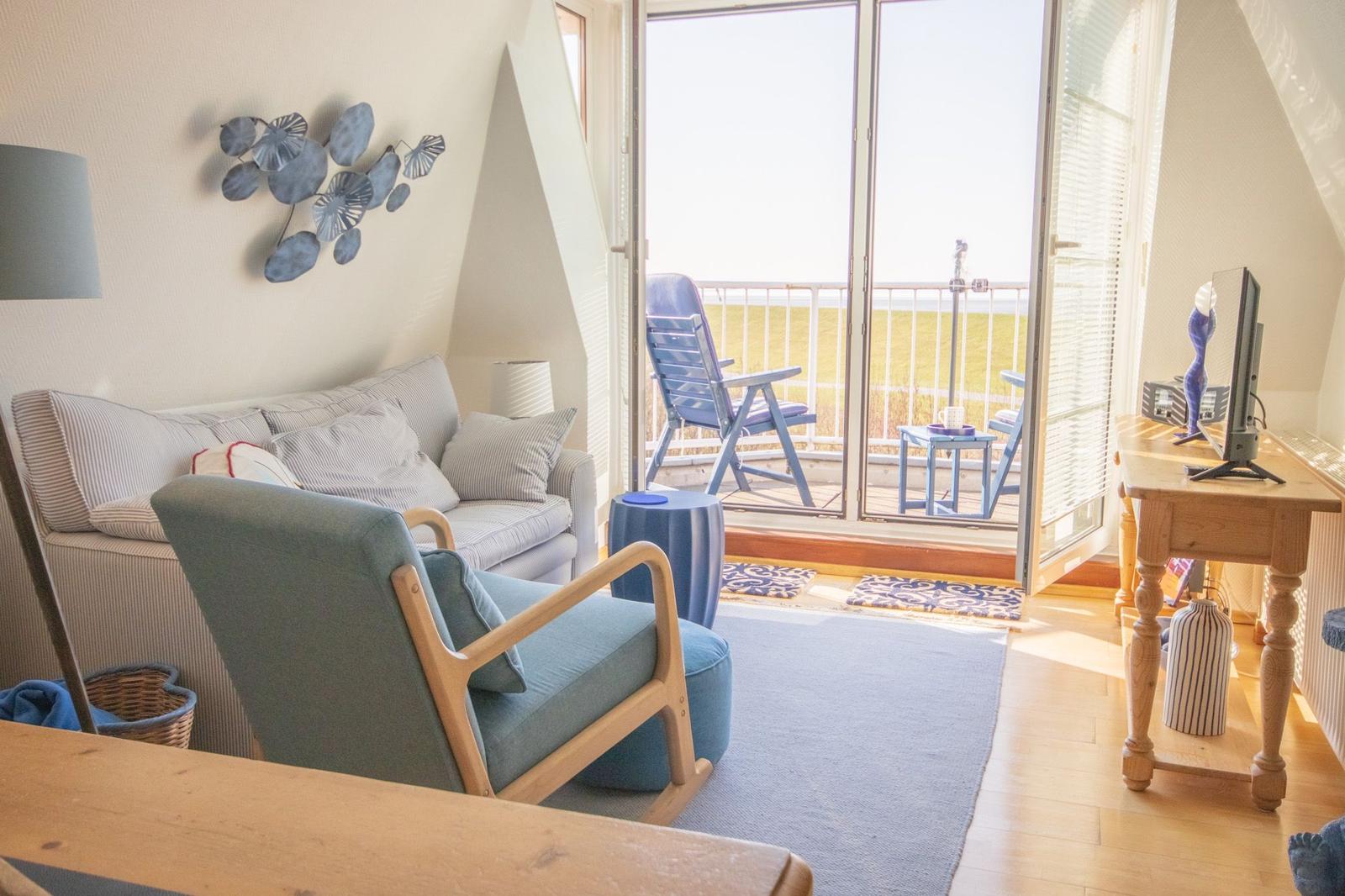 Wohnzimmer mit Sitzgelegenheiten und Balkonblick auf Grasland.