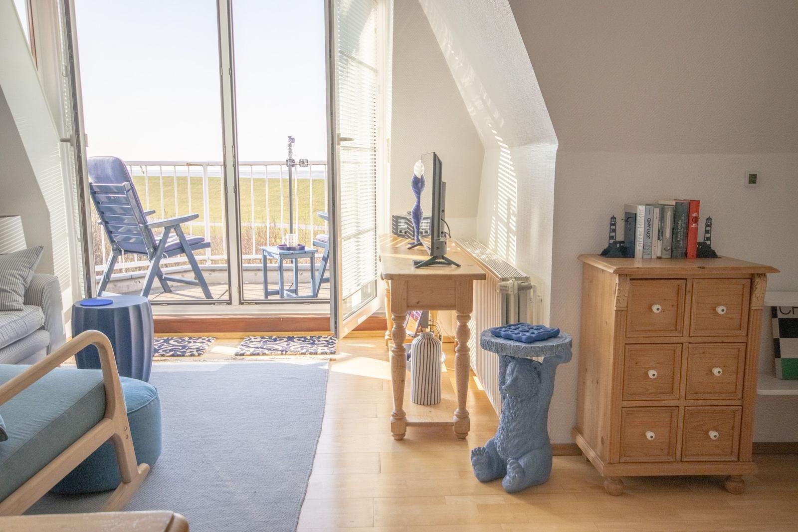 Wohnraum mit Balkon, Schreibtisch, Kommode und blauen Möbeln.