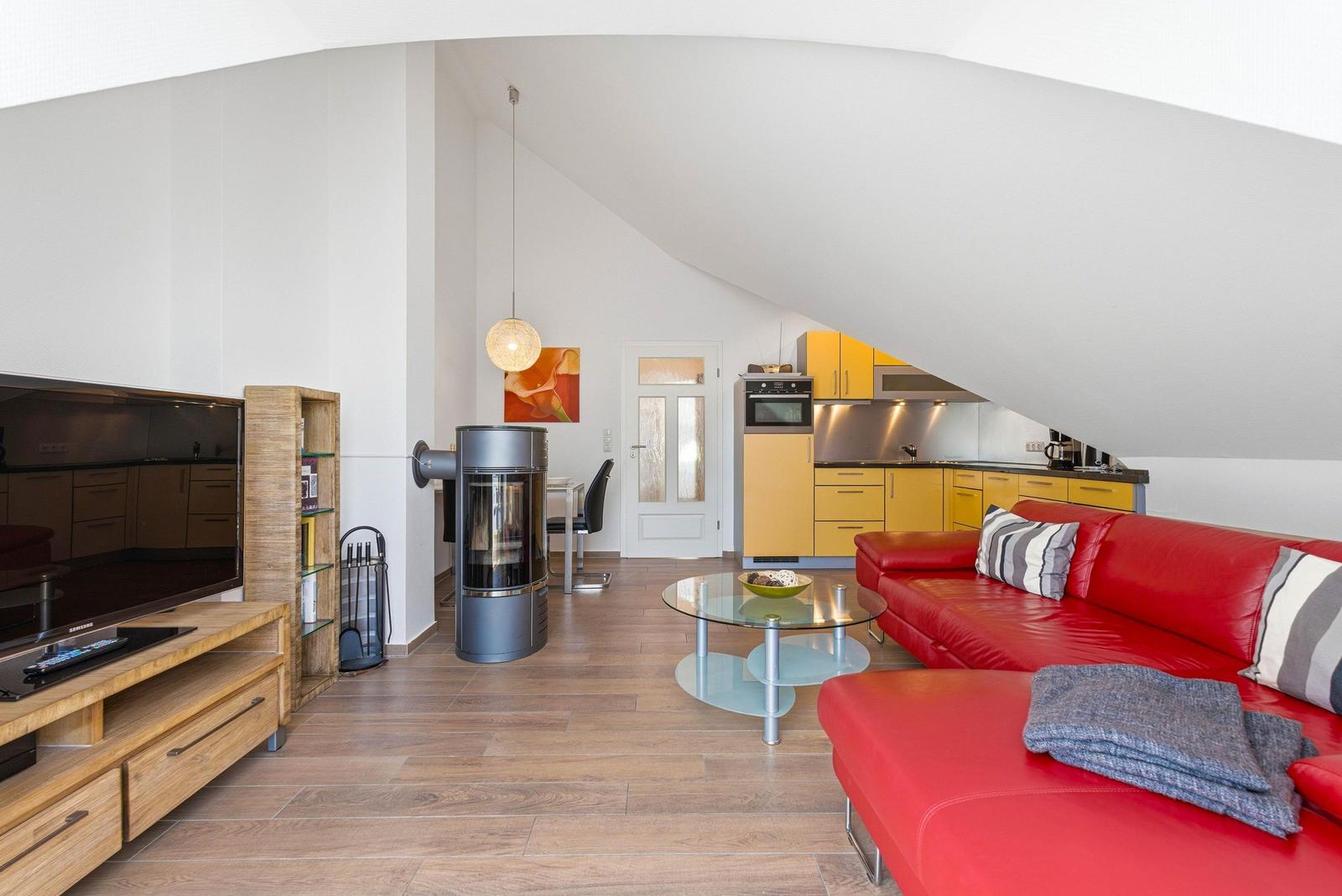 Wohnbereich mit rotem Sofa, Glas-Tisch und Holzboden unter schrägem Dach