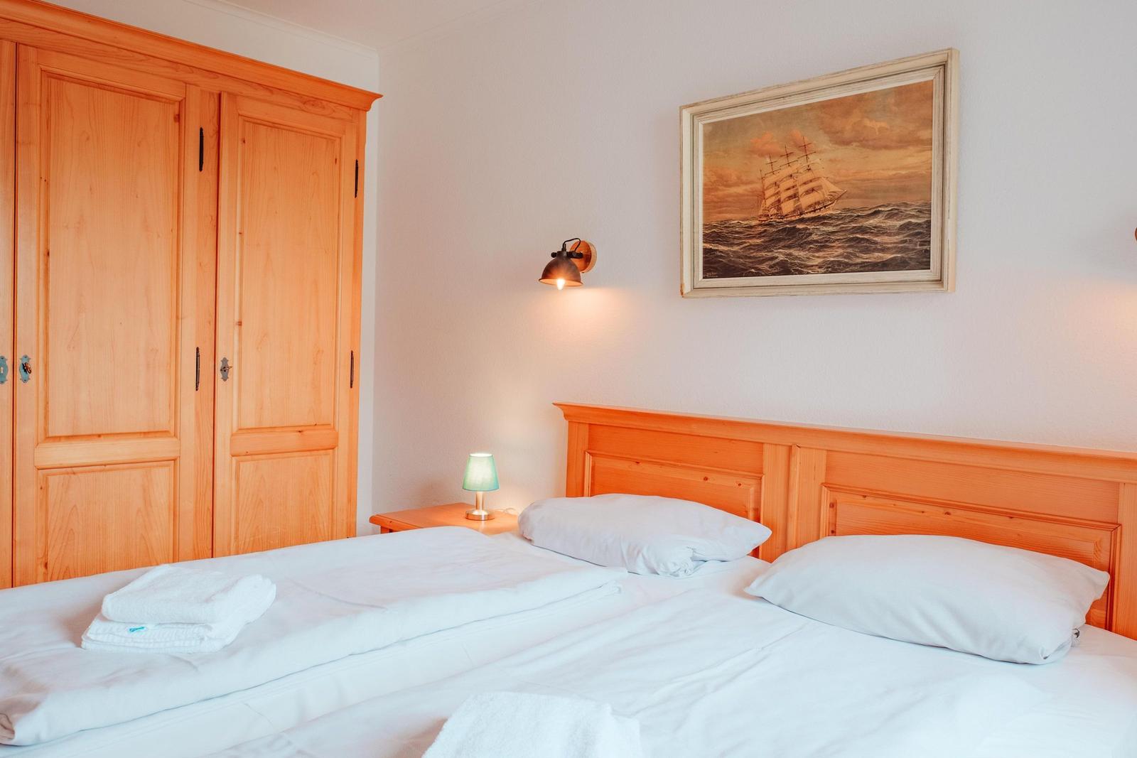 Schlafzimmer mit Holzbett, Kleiderschrank und Wandbild mit Segelschiff.