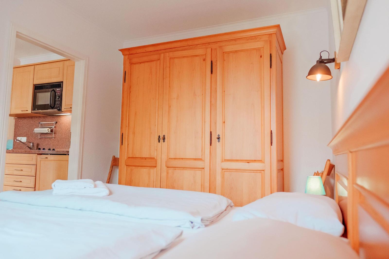Schlafzimmer mit Bett, Holzschrank und Sicht auf Küche