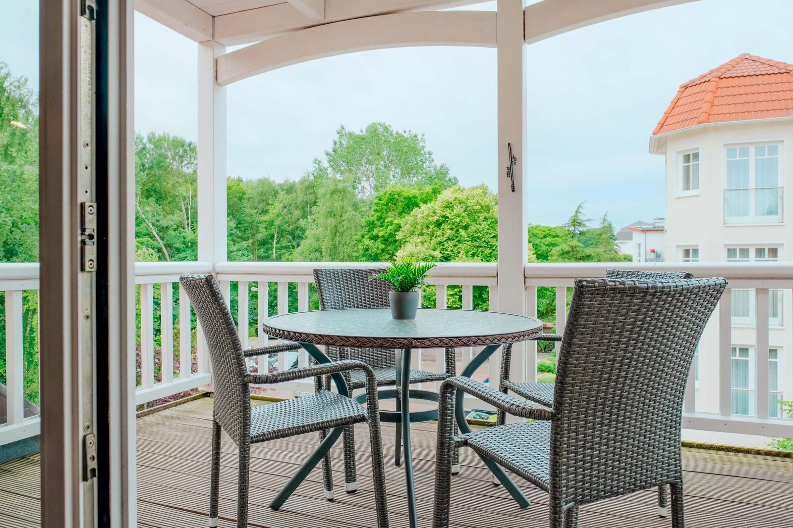 Terrasse mit Tisch und Stühlen, Blick auf grüne Bäume und ein Haus mit rotem Dach.