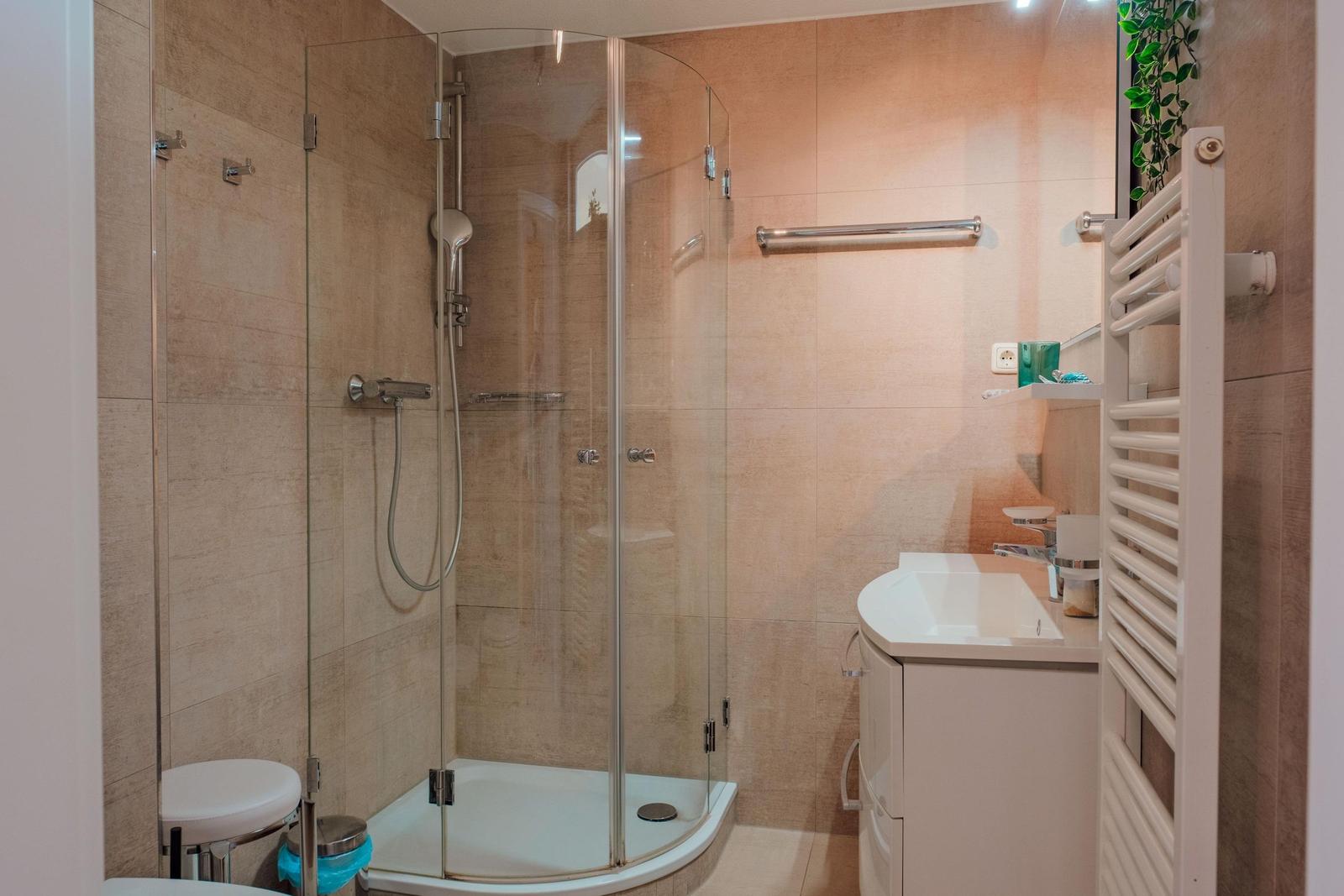 Dusche mit Glaswand, Waschbecken und Heizkörper