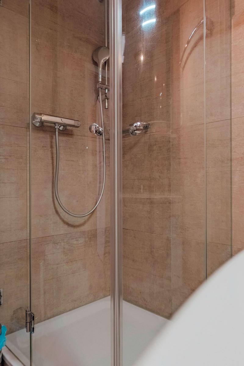 Dusche mit Glaswand und Handbrause, Wandverkleidung aus hellbraunen Fliesen.