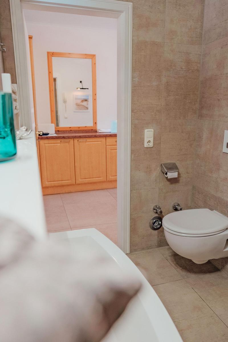 Badezimmer mit Toilette und Blick in den angrenzenden Raum mit Waschbecken und Spiegel.