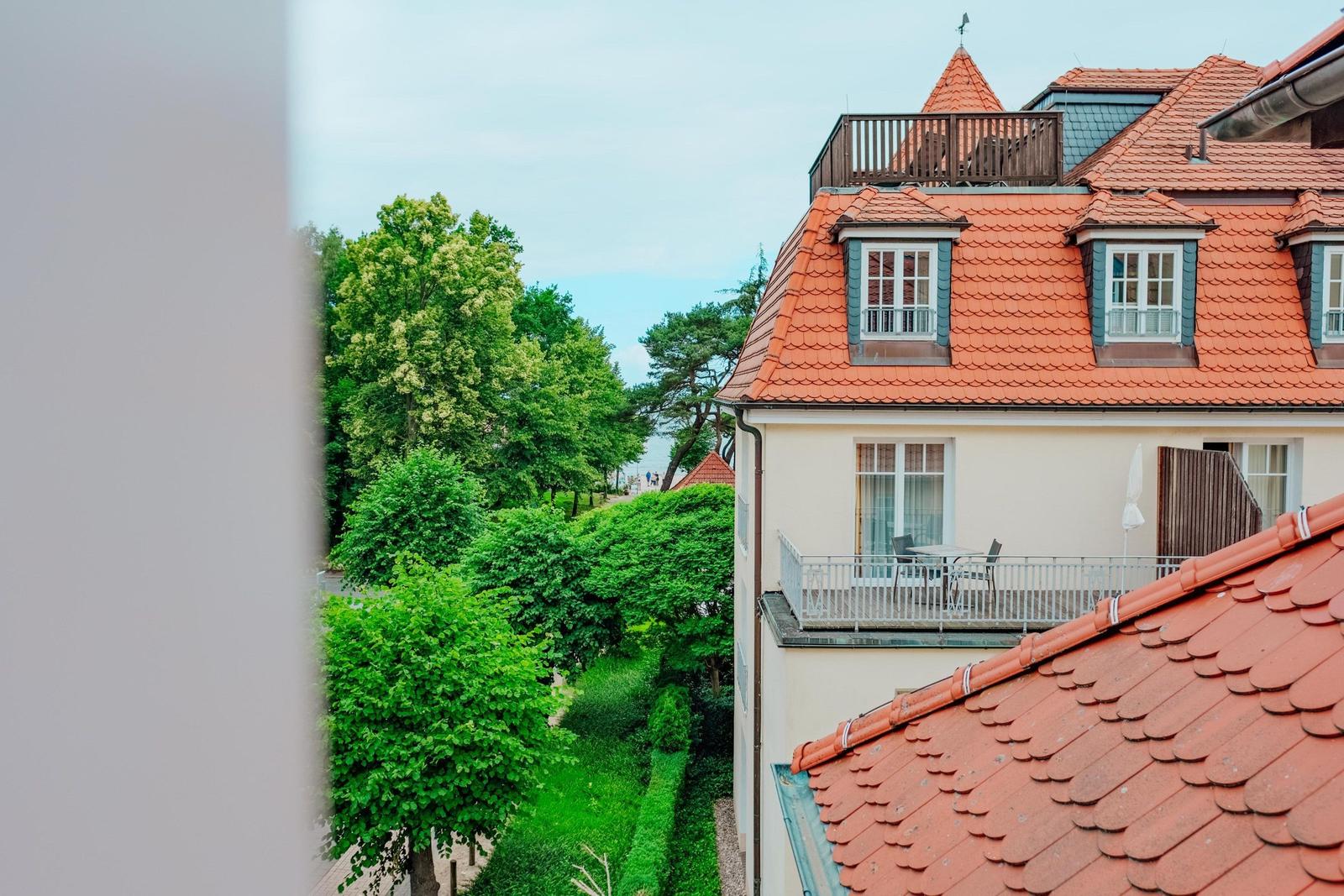 Rotes Dach mit Dachfenstern und Balkon. Grüne Bäume und Gärten im Hintergrund.