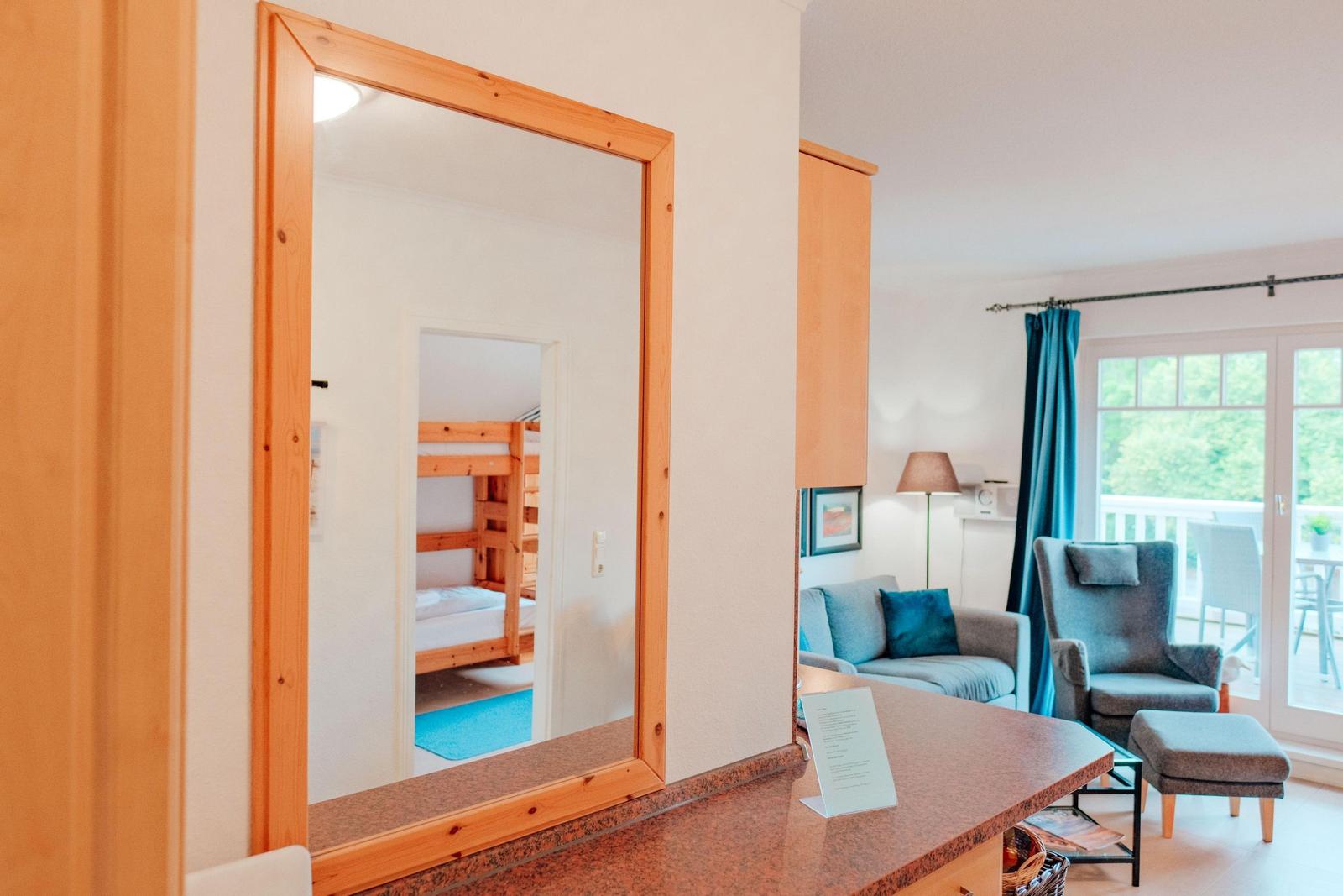 Spiegel zeigt Schlafzimmer mit Doppelstockbett. Wohnbereich mit Sofa, Sessel und Balkon.