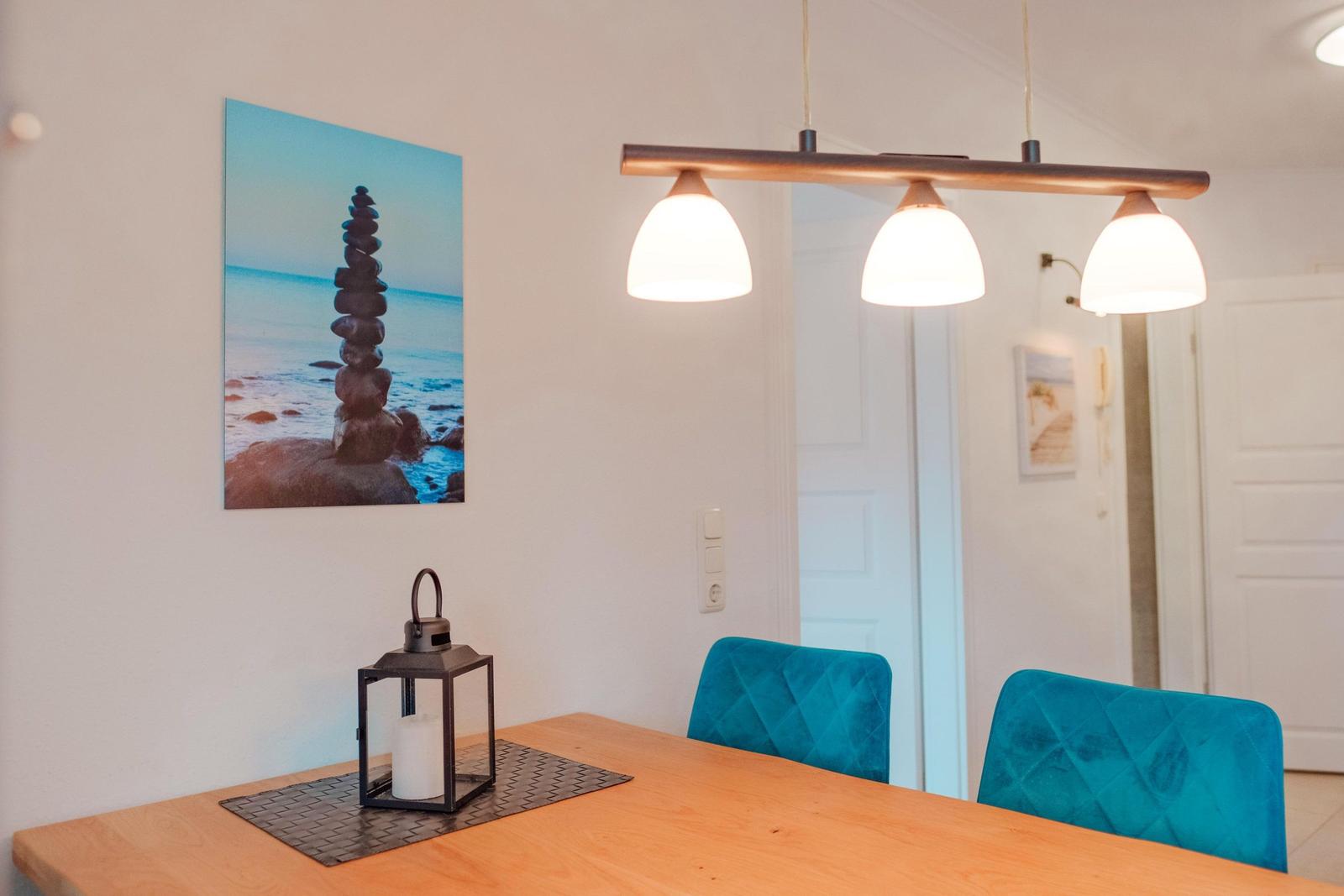 Esstisch mit zwei blauen Stühlen, Wandbild und Hängelampe.