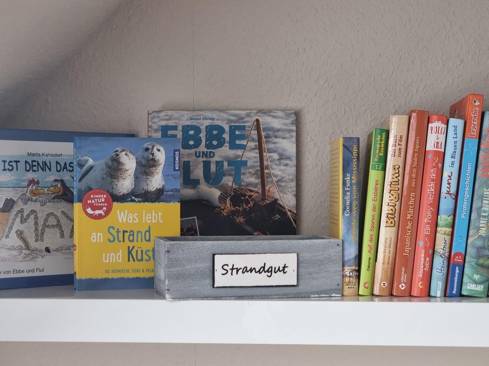 Bookshelf with beach theme and wooden box labeled Strandgut.